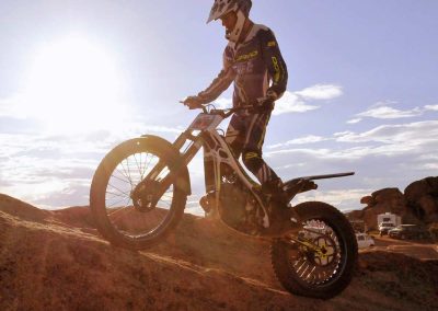 Picture of Evan Manniko riding a trials motorcycle up a slab of rock with the sun behind him.