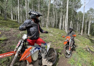 Riders on dirtbike guided rides in colorado come out of an aspen forest.