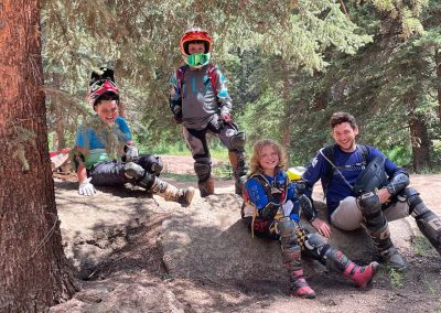 4 Dirtbikers, all kids sitting on rocks in the shade of a Ponderosa in Pike National Forest