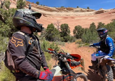 dirtbike tour picture with giant curved red and tan sandstone rock formation in the background