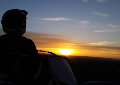 Picture from over the shoulder of a dirt biker, Ian Leeming, with a bright sunset in the distance.