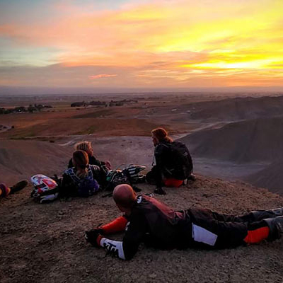 Picture of dirtbikers lying on the ground atop a hill, basking in a warm sunset. 